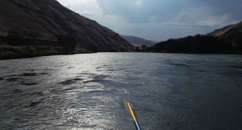 a paddle stretches out over water with tall hills on either side